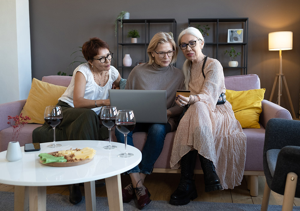 3 ältere Damen sitzen mit Laptop auf der Couch und betrachten eine Bankkarte.