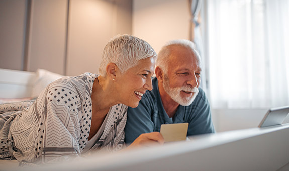 Älteres Paar schaut lächelnd auf einen Computerbildschirm.