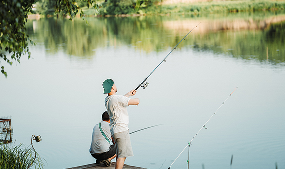 Zwei junge Männer stehen auf einem Steg und angeln am See.