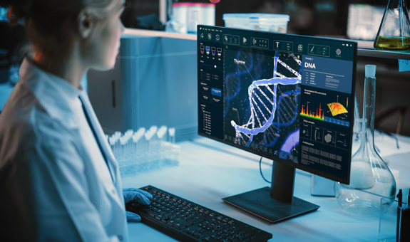 Blonde Frau sitzt in einem Labor vor einem Bildschirm und betrachtet eine DNA Struktur.