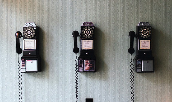 Drei alte Telefone mit Drehschreibe hängen an der Wand.