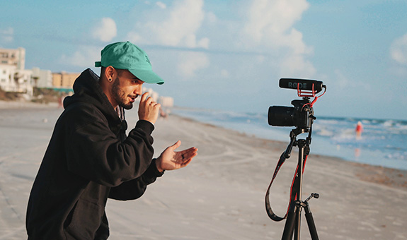Junger Mann mit Pulli performed vor einer Kamera auf Stativ am Strand.