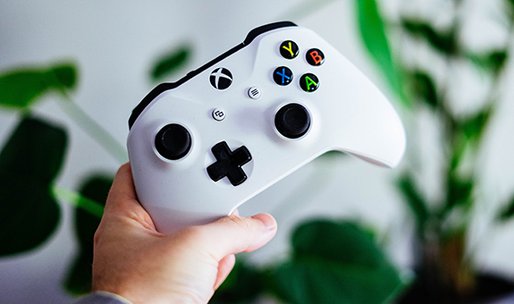 Weißer Xbox remote Kontroller wird von einem Mann vor einer weißen Wand mit grünen Pflanzen gehalten.